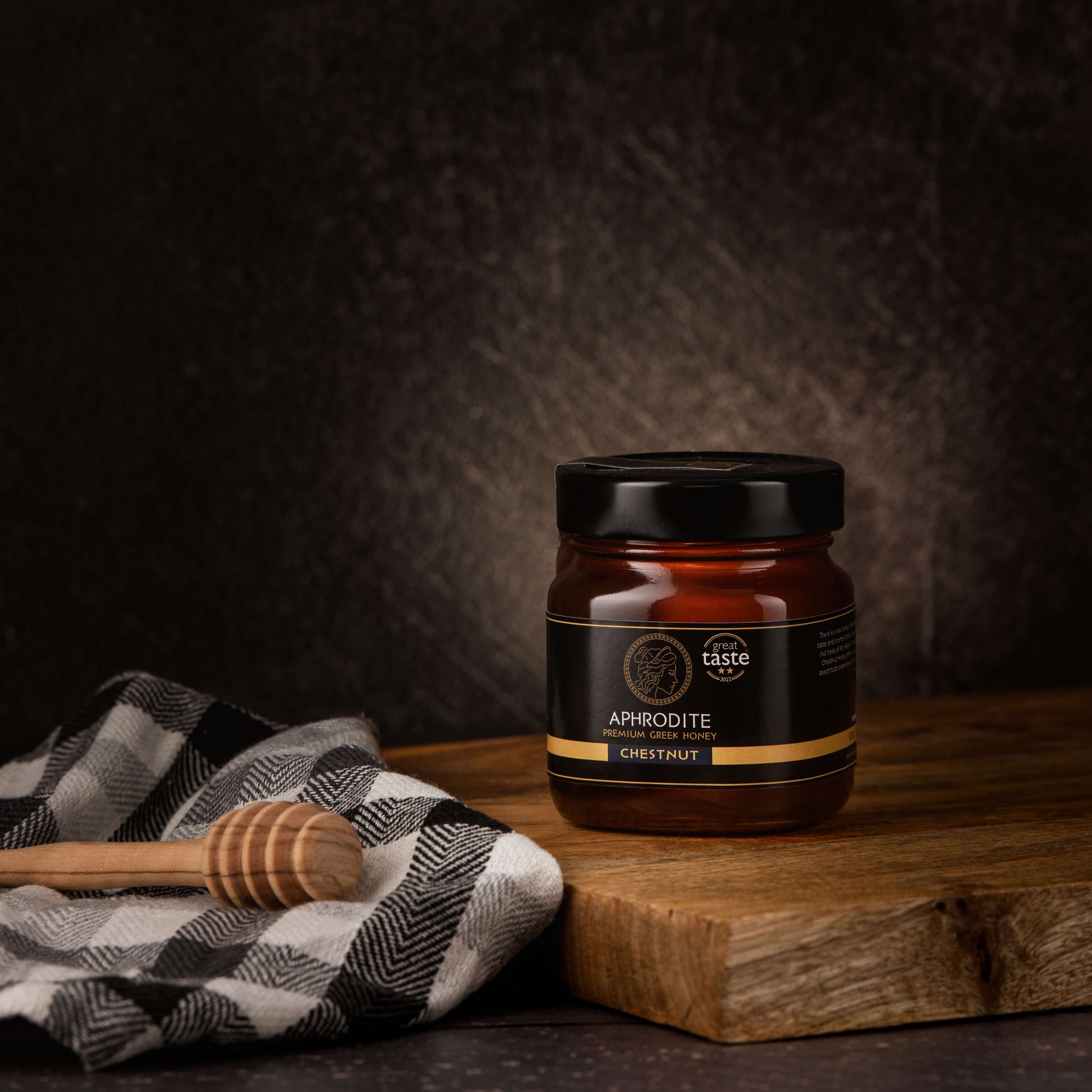 Greek Raw Chestnut Honey in a 250g glass jar in dark / black background. Jar presented on the side. 100% Pure Honey. Aphrodite Honey. Aphrodite Premium Greek Honey. Great Taste 2 stars.