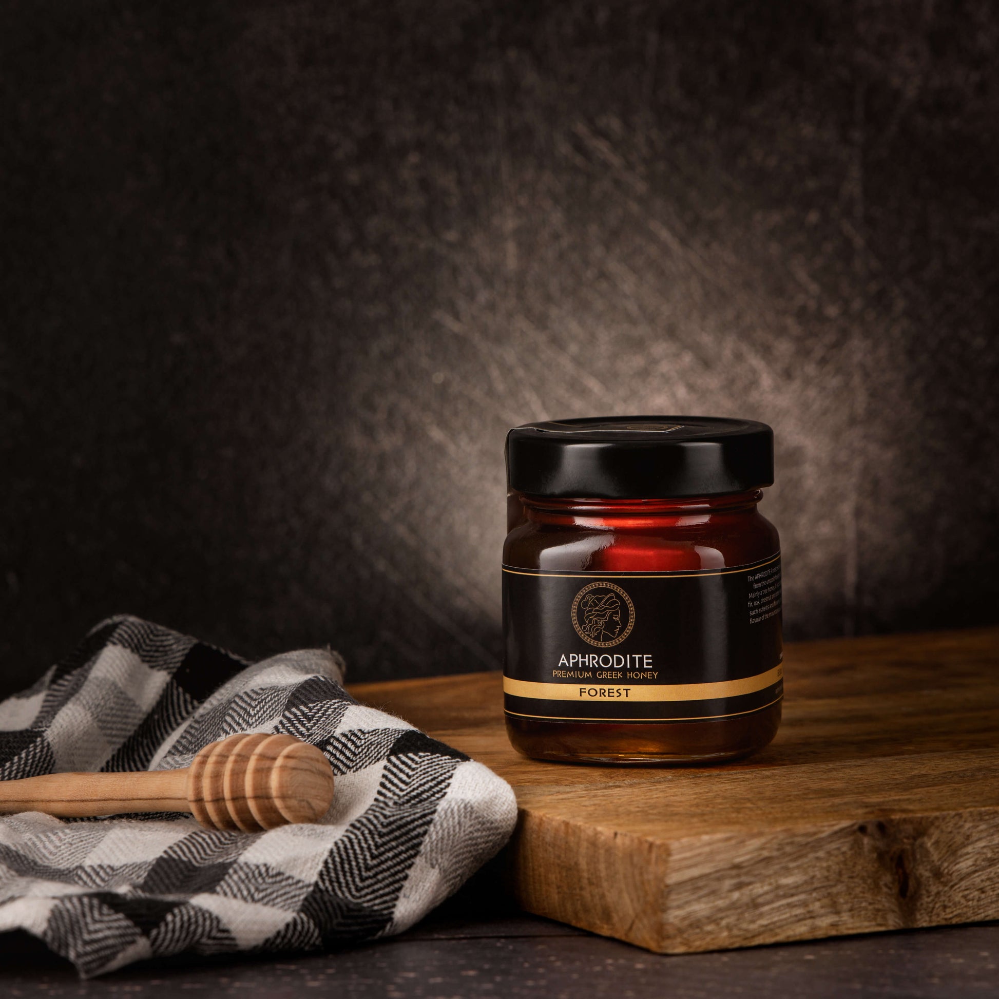Greek Raw Forest Honey in a 250g glass jar in dark / black background. Jar presented on the side. 100% Pure Honey. Aphrodite Honey. Aphrodite Premium Greek Honey.