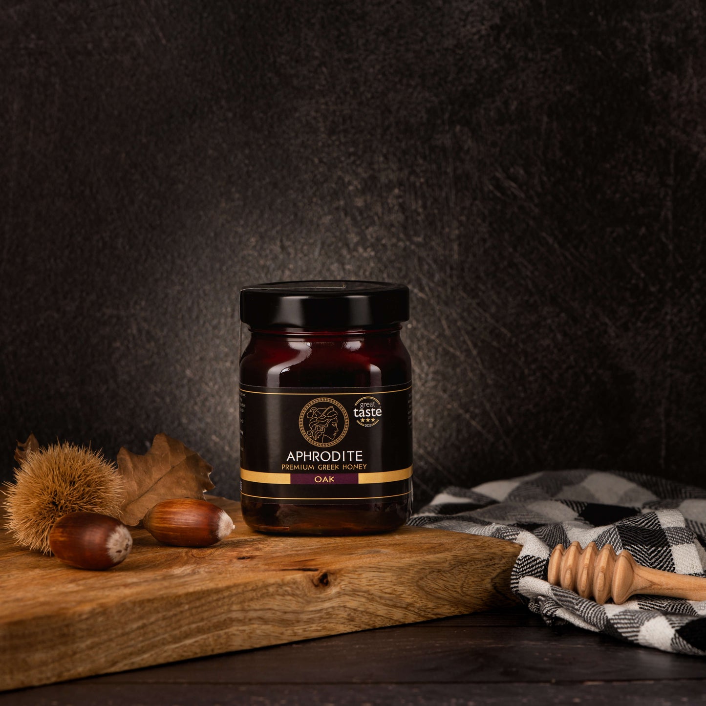 Greek Raw Oak Honey in a 500g glass jar in dark / black background. Jar presented from the front . Oak acorns on the side. 100% Pure Honey. Aphrodite Honey. Aphrodite Premium Greek Honey. Great Taste 3 stars.