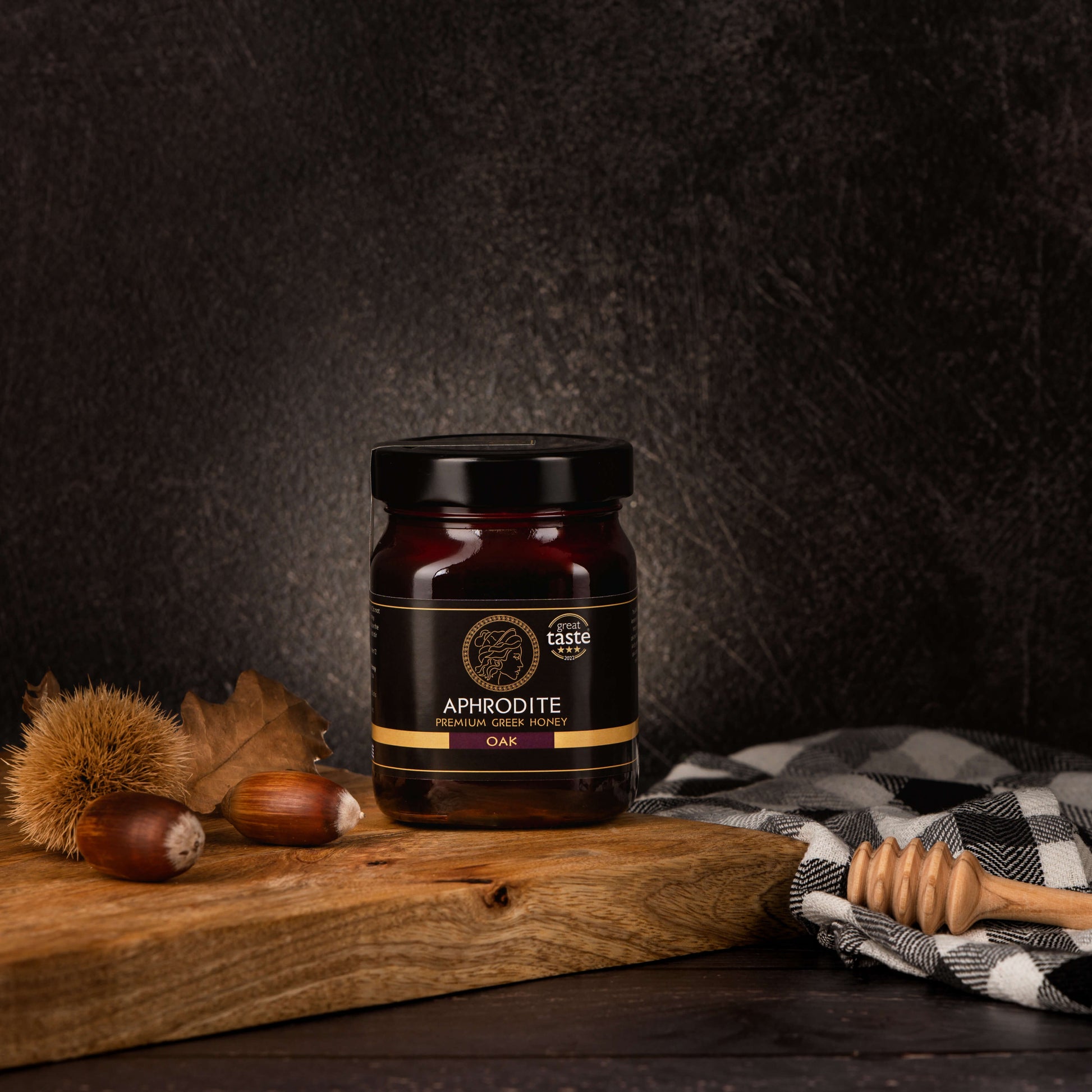 Greek Raw Oak Honey in a 500g glass jar in dark / black background. Jar presented from the front . Oak acorns on the side. 100% Pure Honey. Aphrodite Honey. Aphrodite Premium Greek Honey. Great Taste 3 stars.