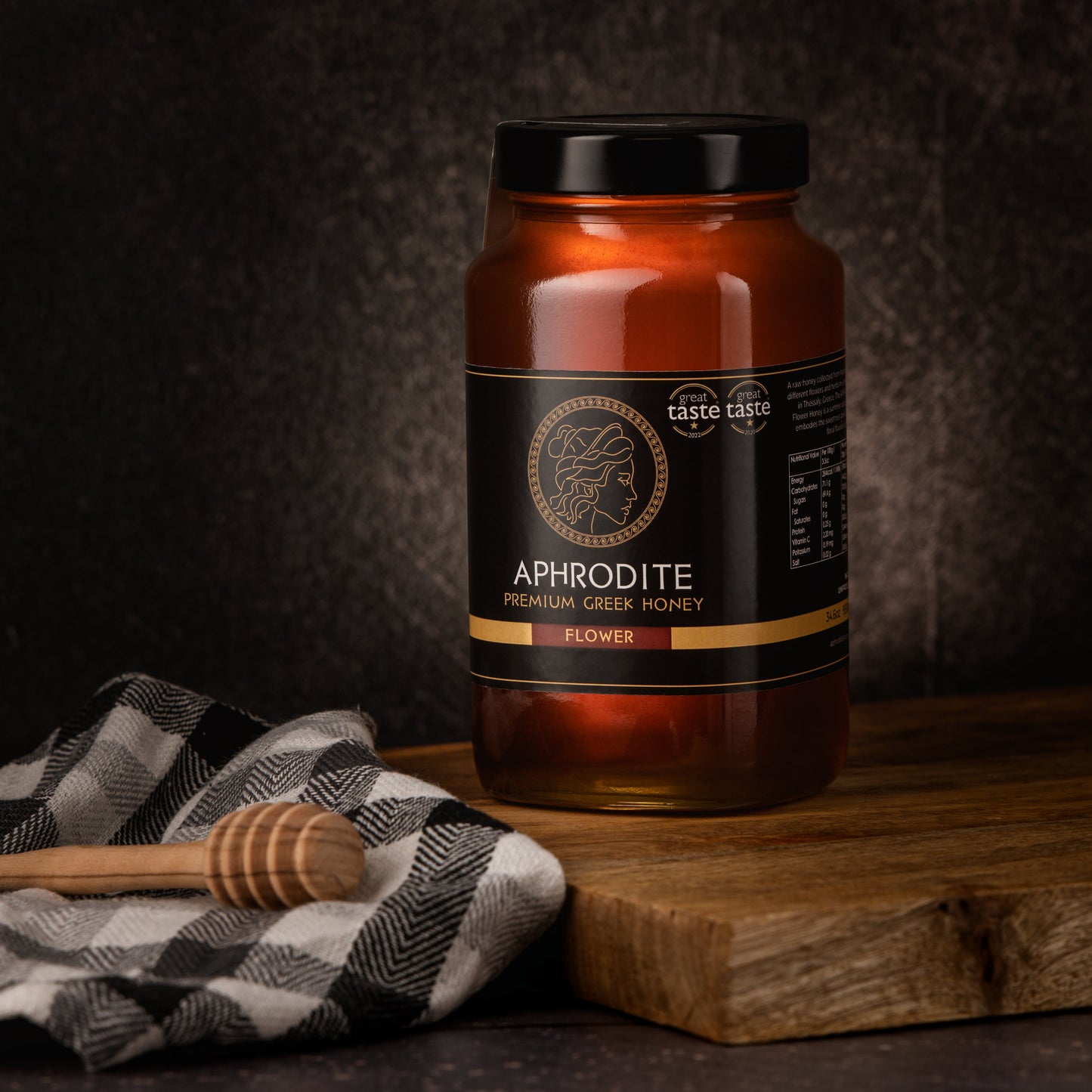 Greek Raw Flower / Blossom Honey in a 950g glass jar in dark / black background. Jar presented on the side. 100% Pure Honey. Aphrodite Honey. Aphrodite Premium Greek Honey. Great Taste 1 star.