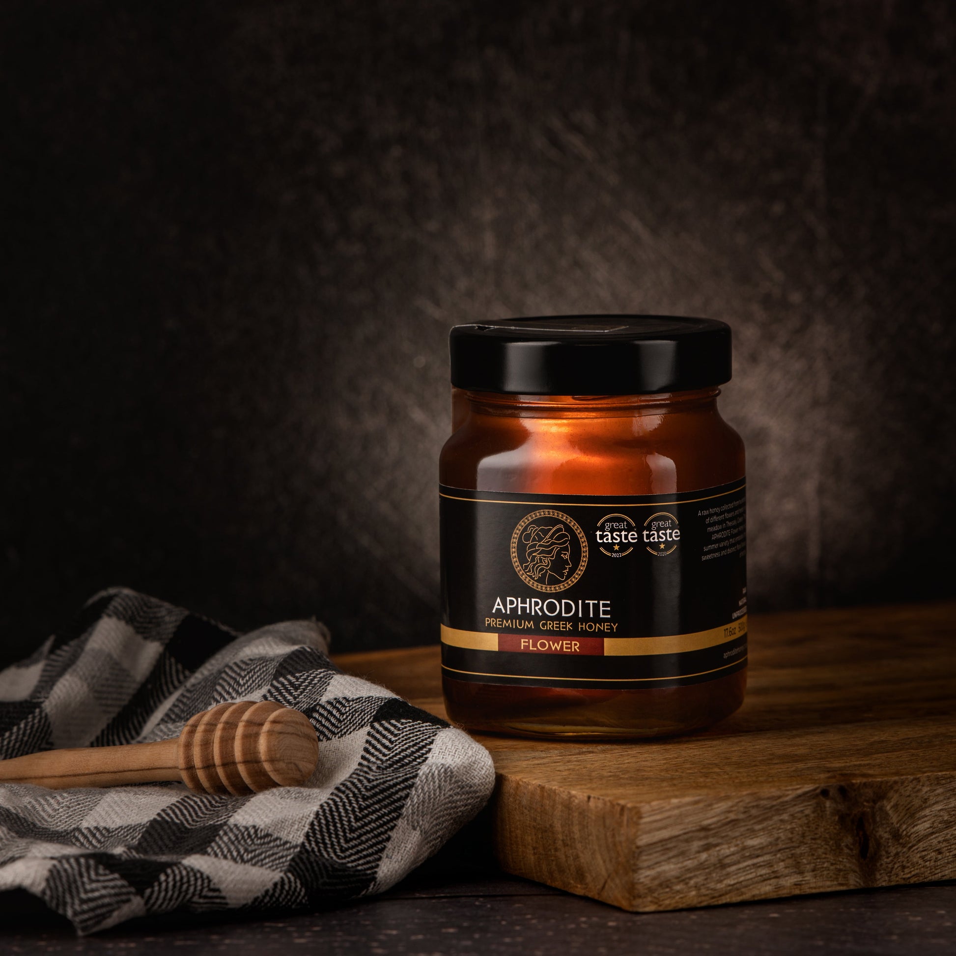 Greek Raw Flower / Blossom Honey in a 500g glass jar in dark / black background. Jar presented on the side. 100% Pure Honey. Aphrodite Honey. Aphrodite Premium Greek Honey. Great Taste 1 star.