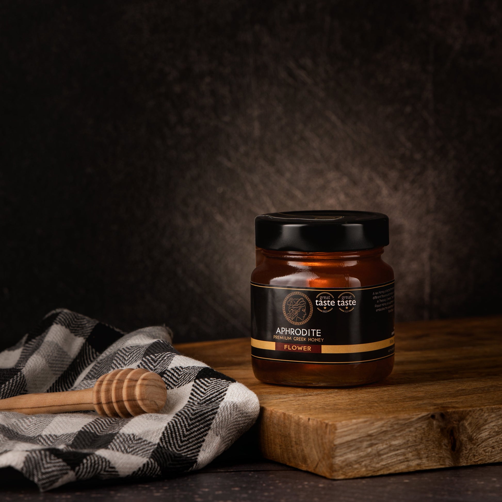 Greek Raw Flower / Blossom Honey in a 250g glass jar in dark / black background. Jar presented on the side. 100% Pure Honey. Aphrodite Honey. Aphrodite Premium Greek Honey. Great Taste 1 star.