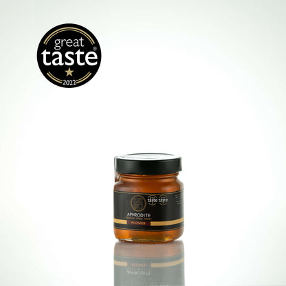 Aphrodite Raw Flower Honey 250g glass jar with black lid on a white reflective background, Great Taste 2022 award badge
