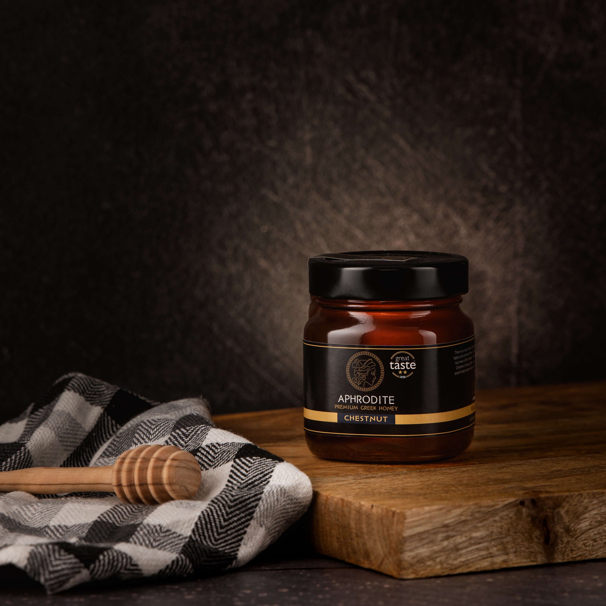Aphrodite Raw Chestnut Honey 250g jar on wooden board with checkered cloth and wooden honey dipper