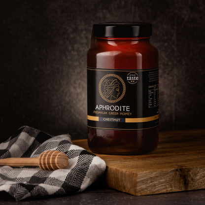 Greek Raw Chestnut Honey in a 950g glass jar in dark / black background. Jar presented on the side. 100% Pure Honey. Aphrodite Honey. Aphrodite Premium Greek Honey. Great Taste 2 stars.