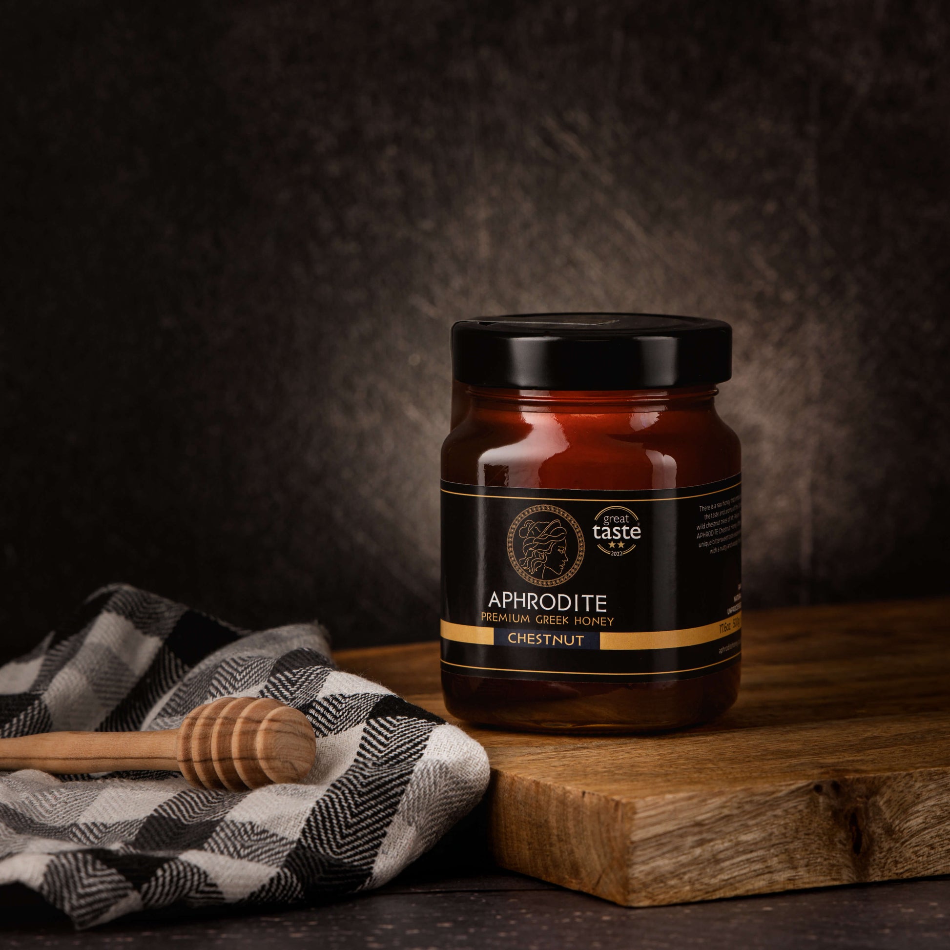 Greek Raw Chestnut Honey in a 500g glass jar in dark / black background. Jar presented on the side. 100% Pure Honey. Aphrodite Honey. Aphrodite Premium Greek Honey. Great Taste 2 stars.