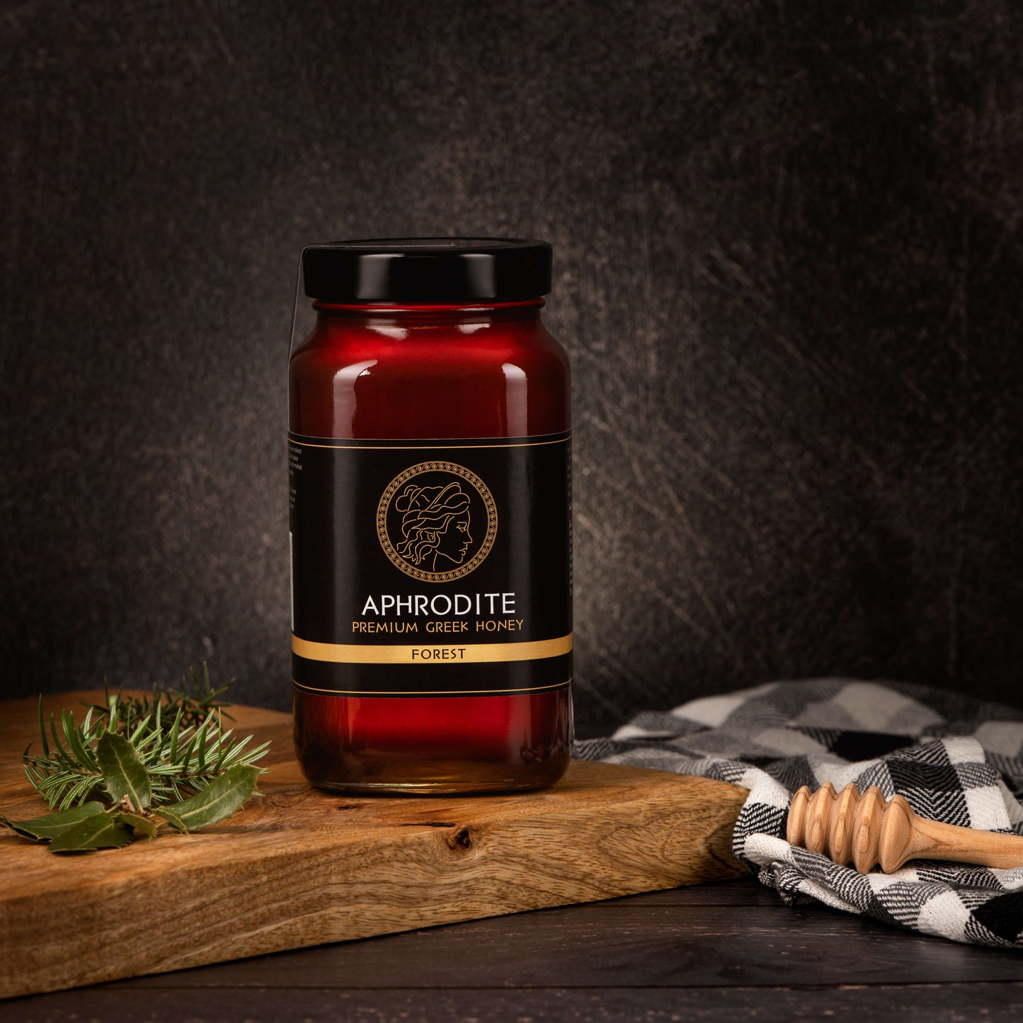 Greek Raw Forest Honey in a 950g glass jar in dark / black background. Jar presented from the front . Tree leaves on the side. 100% Pure Honey. Aphrodite Honey. Aphrodite Premium Greek Honey.