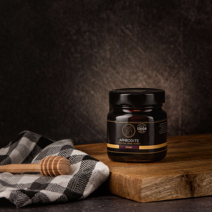 Greek Raw Oak Honey in a 250g glass jar in dark / black background. Jar presented on the side. 100% Pure Honey. Aphrodite Honey. Aphrodite Premium Greek Honey. Great Taste 3 stars.